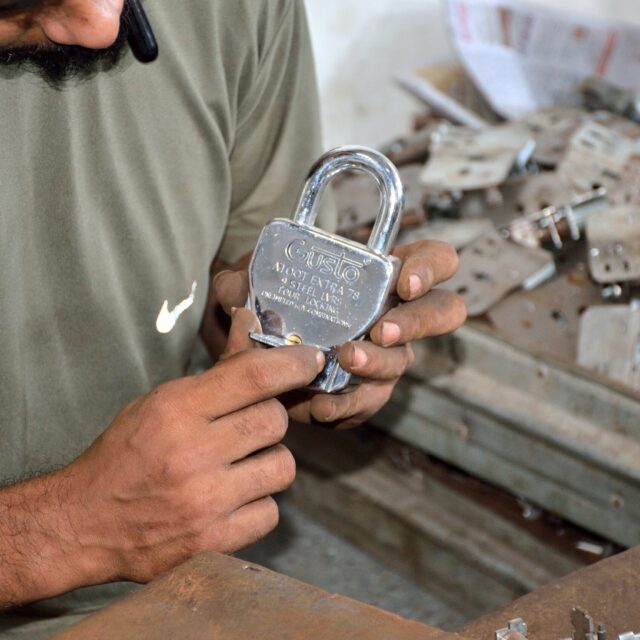 A worker holding up a finished chrome padlock to inspect it