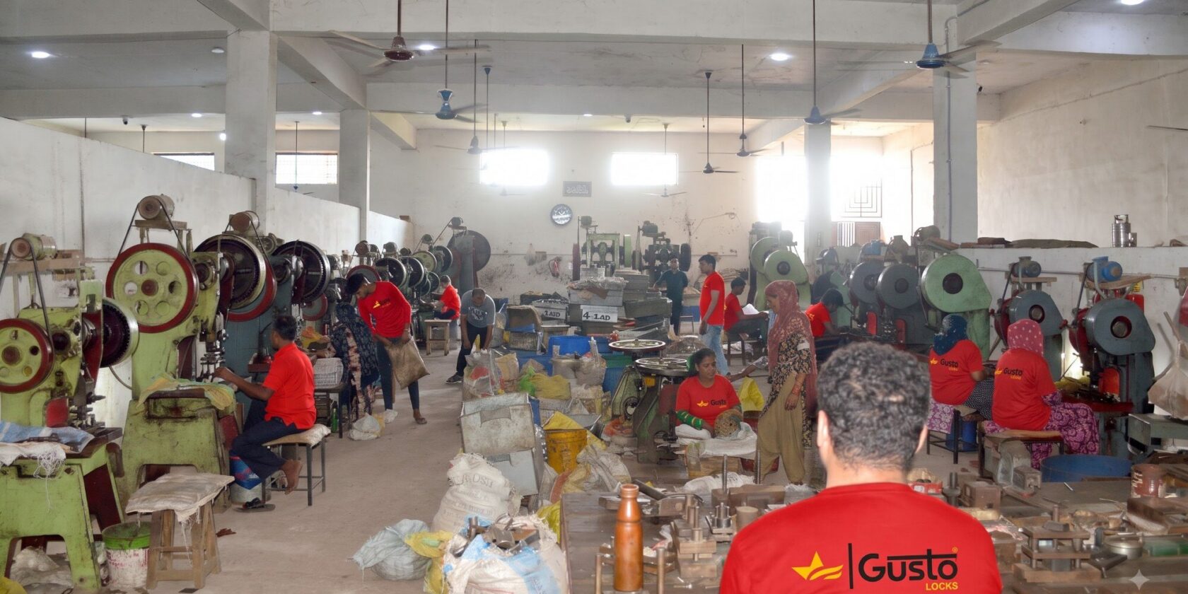 Rows of power presses worked by operators in Gusto Locks uniform on the factory floor in Aligarh
